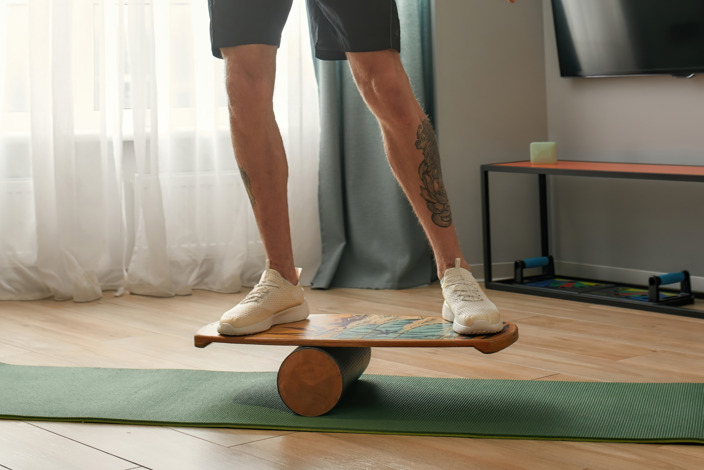 Mann surft auf Balance Board auf Yogamatte im Wohnzimmer