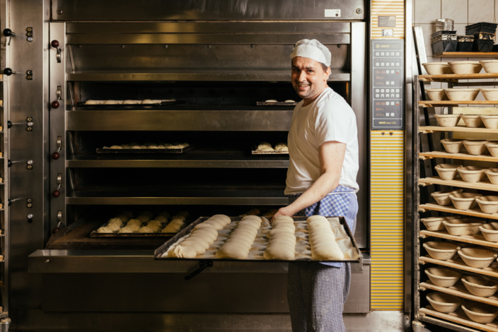 Bäcker in Goldbrötchen Bäckerei holt Brötchen aus dem Ofen