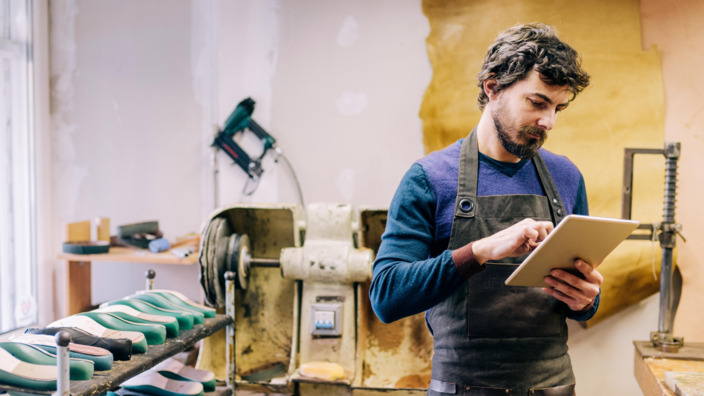 Handwerker steht in Werkstatt und arbeitet am Tablet