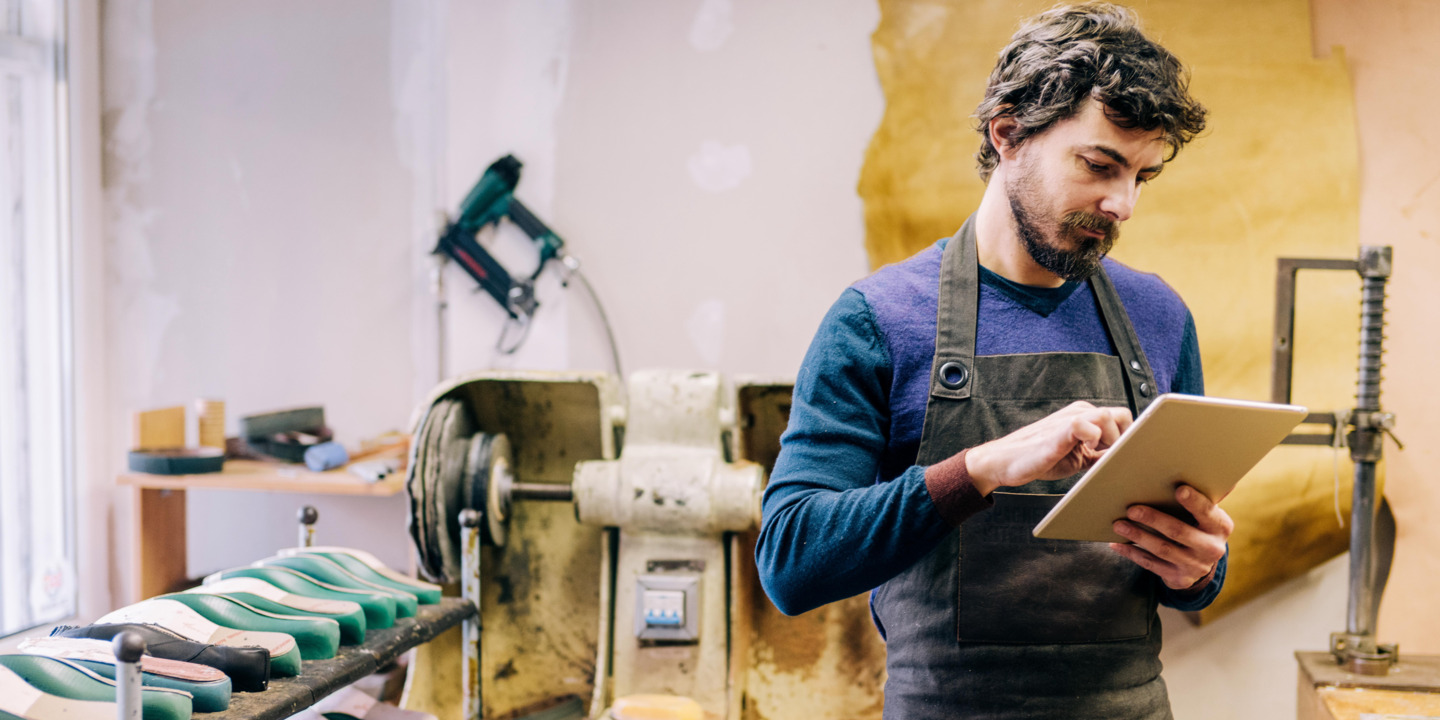 Handwerker steht in Werkstatt und arbeitet am Tablet