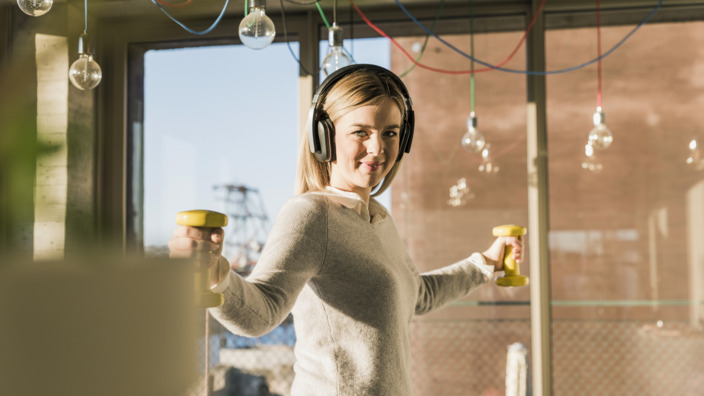 Frau mit Kopfhörern, die Hanteln in der Hand hält 
