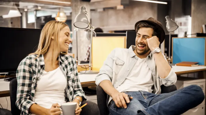 Ein Mann und eine Frau sitzen im Büro und lachen gemeinsam.