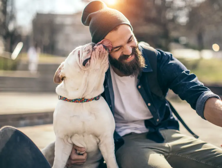Mann wird von seinem Hund über das Gesicht geleckt.
