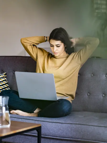 Junge Frau sitzt auf Sofa und übt am Computer Microjob aus