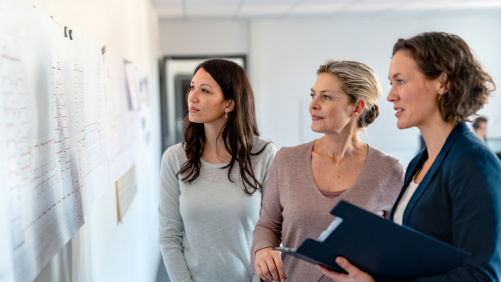 3 Frauen, die auf eine Pinnwand schauen