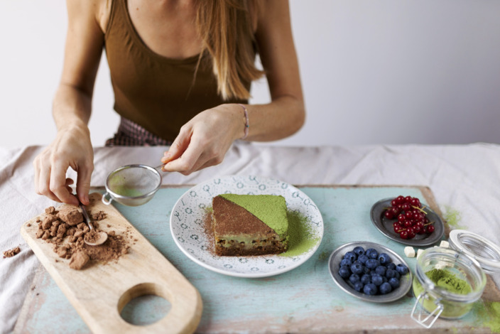 Frau dekoriert veganen Kuchen mit Matcha und Kakaopulver