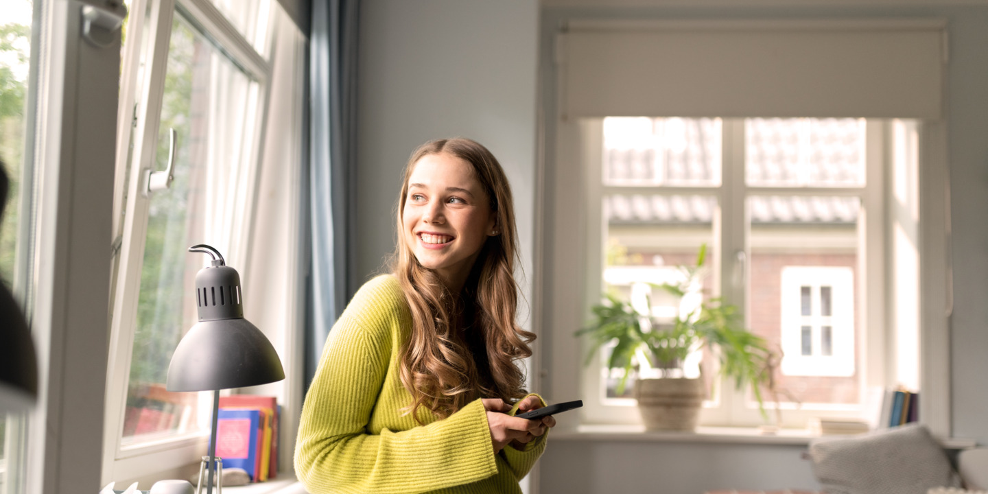 Junge Frau schaut neugierig aus dem Fenster.