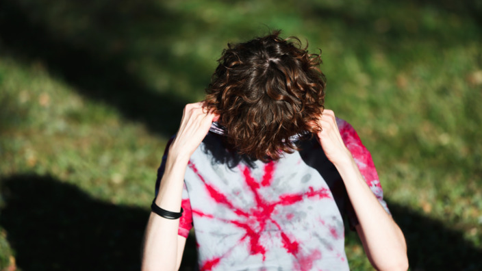 Junger Mensch sitzt auf der Wiese und steckt den Kopf ins T-Shirt