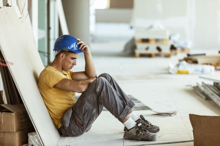 Handwerker mit Burn-out sitzt niedergeschlagen am Boden