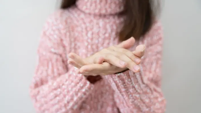 Eine Frau in einem rosa Rollkragenpullover mit ineinander gelegten Händen.