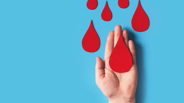 Bluttropfen aus rotem Filz auf Hand vor blauem Hintergrund.