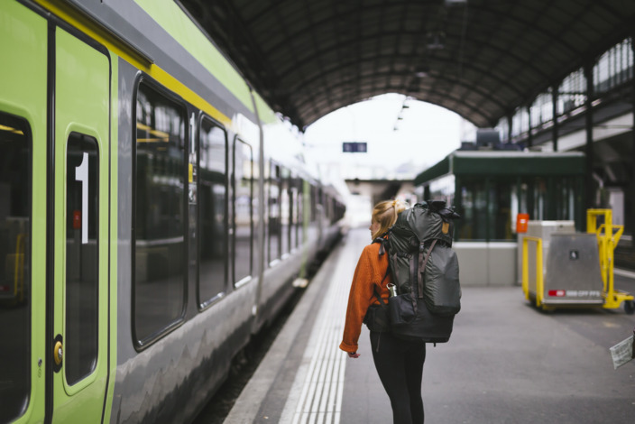 Backpackerin steht am Gleis im Bahnhof