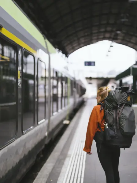 Backpackerin steht am Gleis im Bahnhof