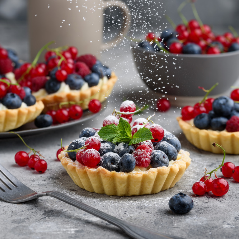 Mehrere Beeren-Tartlettes werden mit Puderzucker bestäubt