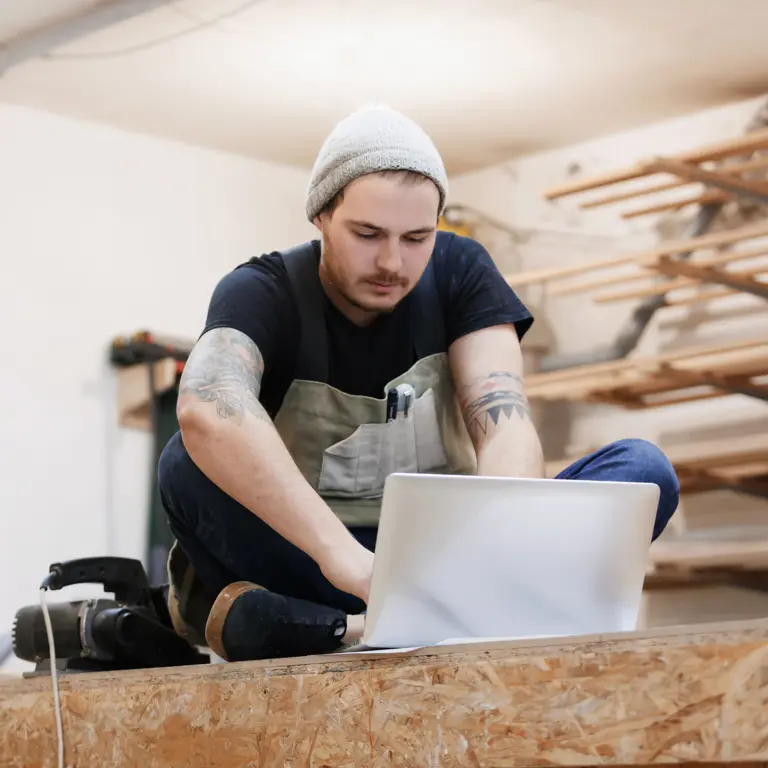 Junger Handwerker füllt Berichtsheft am Laptop aus
