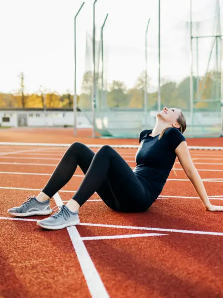 Frau in Sportkleidung sitzt auf Aschebahn des Sportplatzes