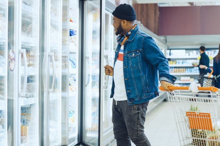 Mann mit Einkaufswagen steht vor Regal im Supermarkt