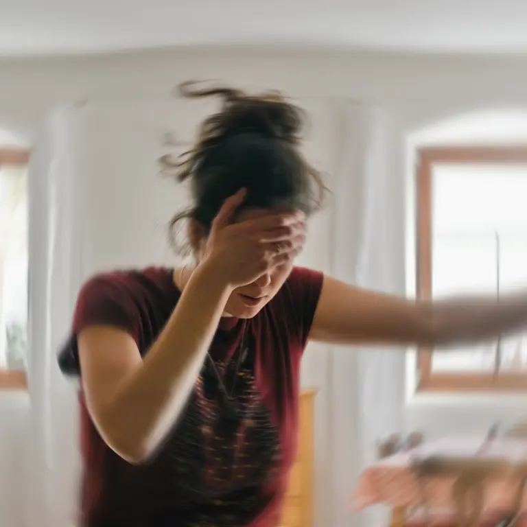 Frau hält sich im Schwindel die Hand vor die Stirn und stützt sich am Türrahmen ab.