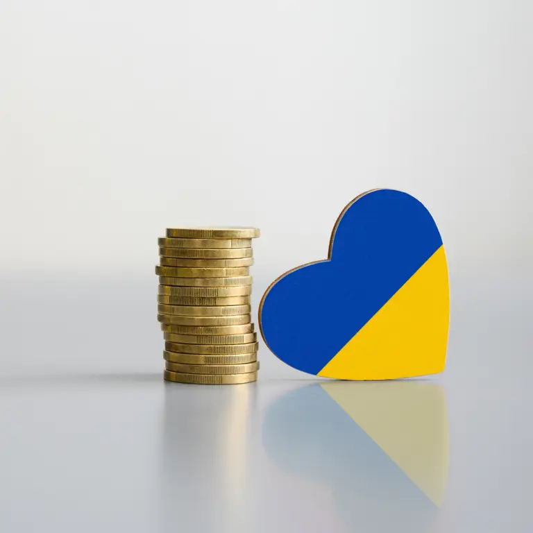 Ein Stapel Münzen und die Flagge der Ukraine in Form eines Herzens