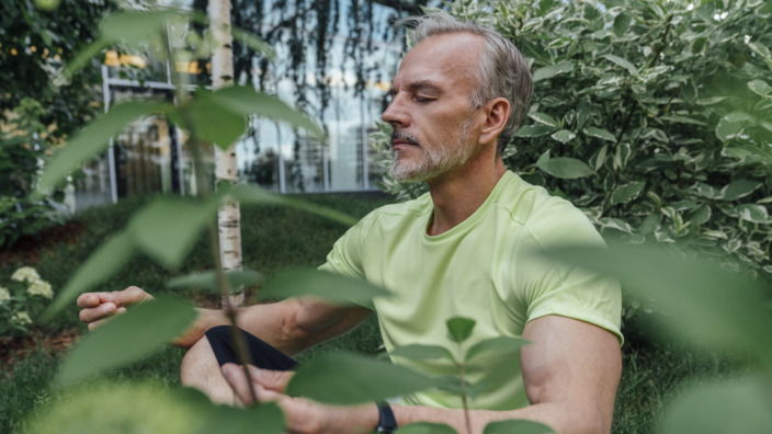 Mann sitzt im Garten und meditiert