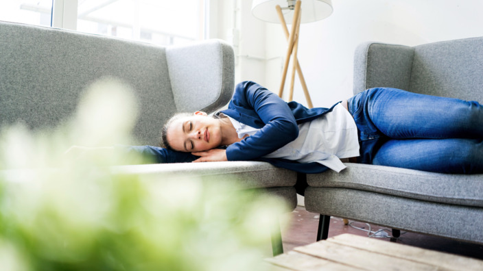 Frau liegt im Büro auf der Couch und ruht sich aus