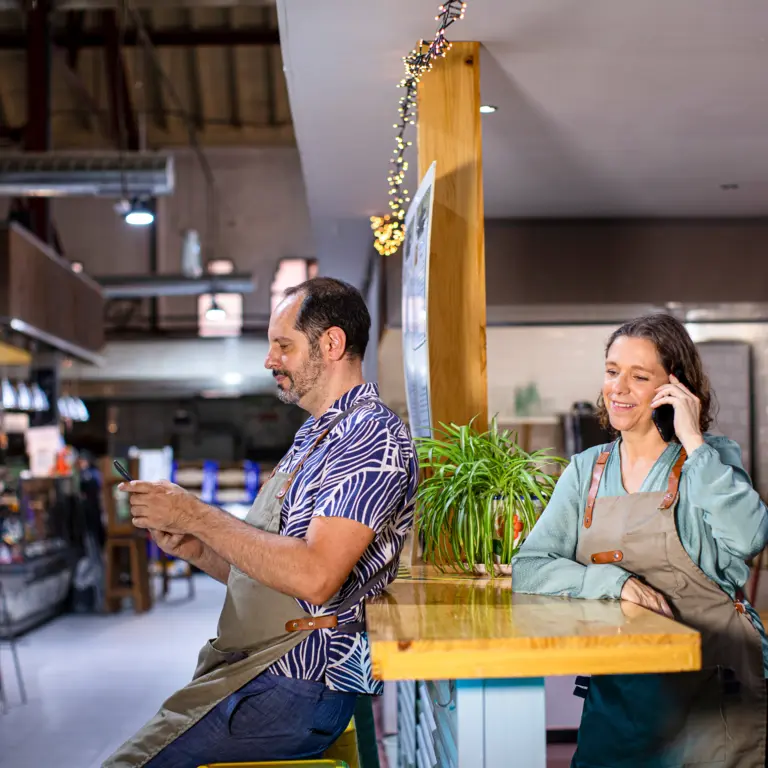 Zwei Kellner:innen stehen im Restaurant und benutzen ihr Smartphone
