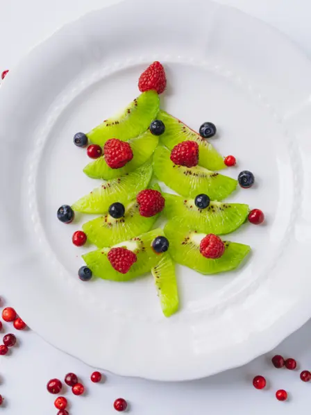 dekorierter Teller mit einem gelegten Tannenbaum aus Kiwi und Beeren