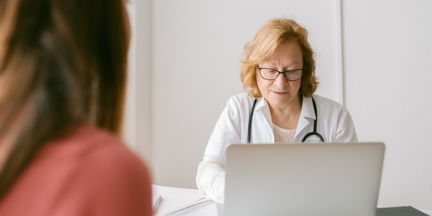 Ärztin sitzt am Laptop und eine Patientin sitzt gegenüber