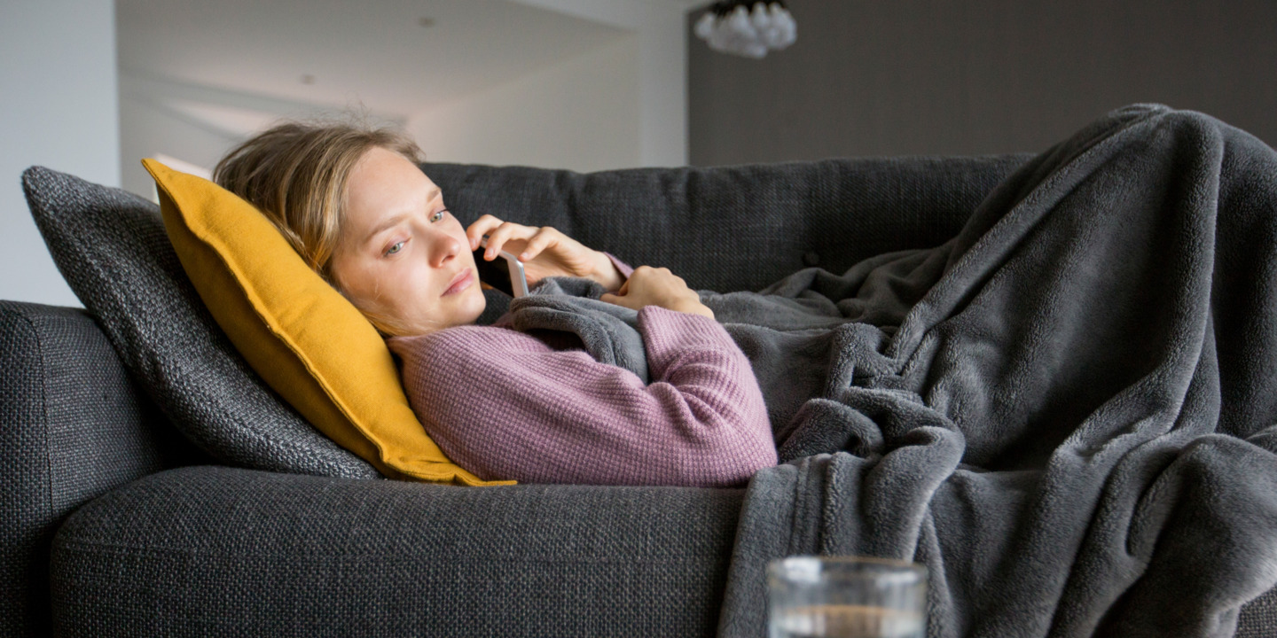 Frau liegt krank auf dem Sofa und telefoniert