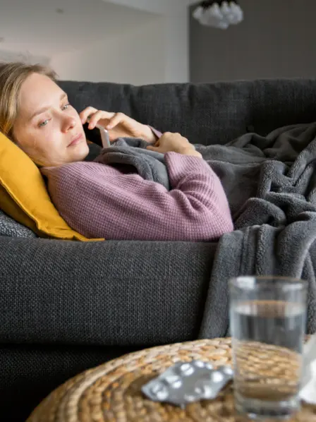 Frau liegt krank auf dem Sofa und telefoniert
