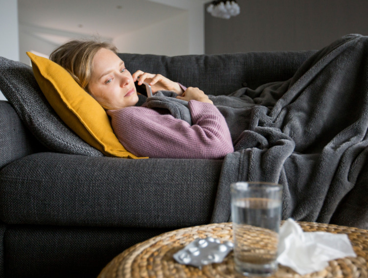 Frau liegt krank auf dem Sofa und telefoniert