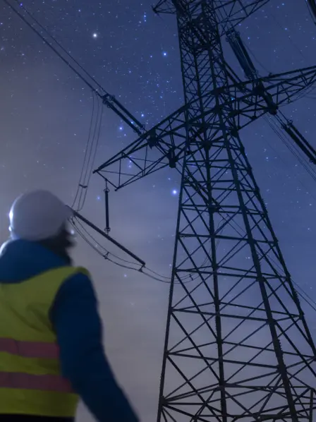 Arbeiter steht in der Nacht mit einer Leuchte vor Strommast.