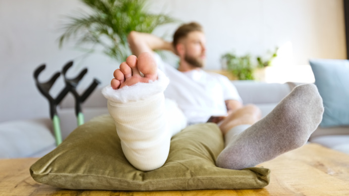 Ein Mann sitzt mit Gipsfuß auf der Couch.