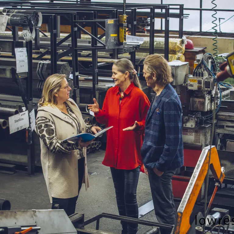Unternehmerpaar spricht mit Mitarbeiterin in Werkshalle