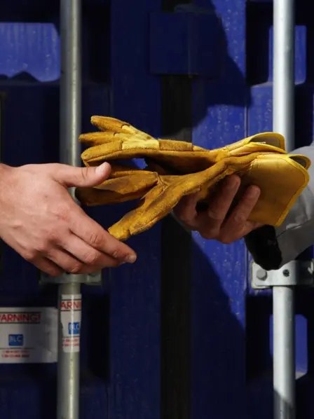 Nahaufnahme wie eine Person der Anderen Arbeitshandschuhe überreicht.