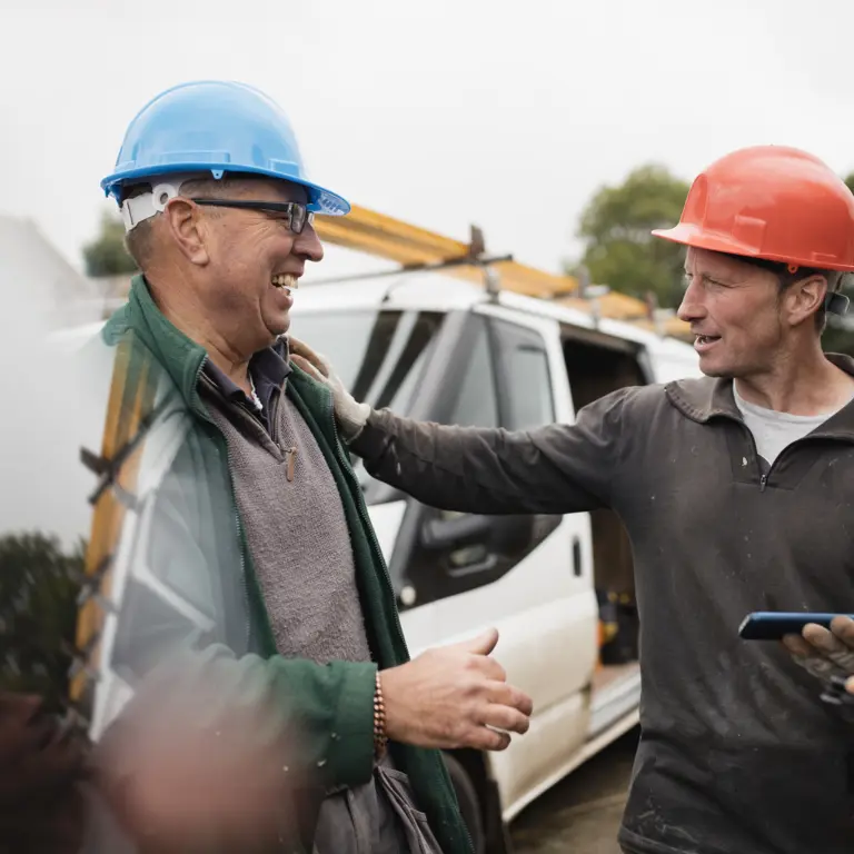 Zwei Handwerker stehen vor ihrem Lieferwagen und lachen miteinander