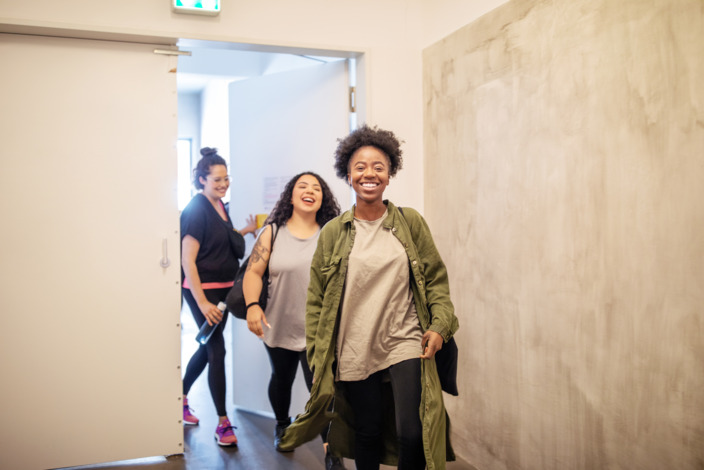 Junge Frauen verlassen lachend zum Feierabend das Büro