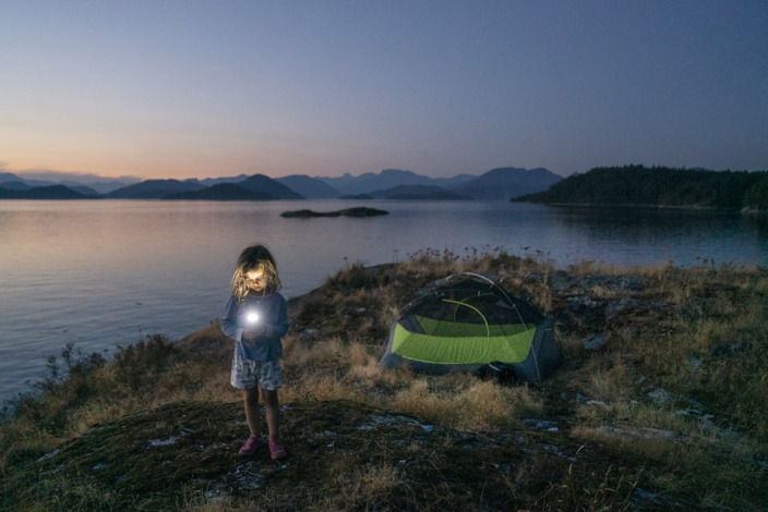 Kind steht mit Taschenlampe am nächtlichen See