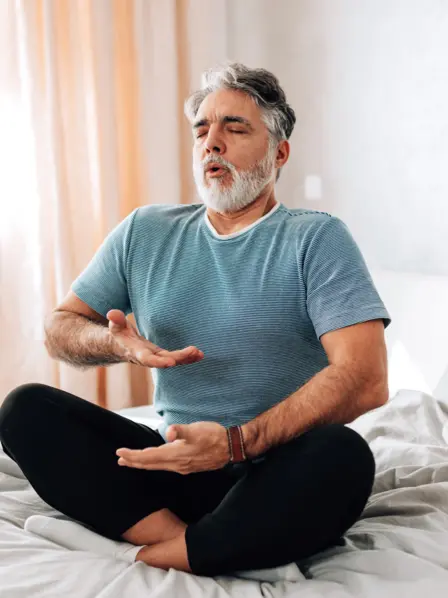 Ein Mann sitzt auf dem Bett und macht Atemübungen. 