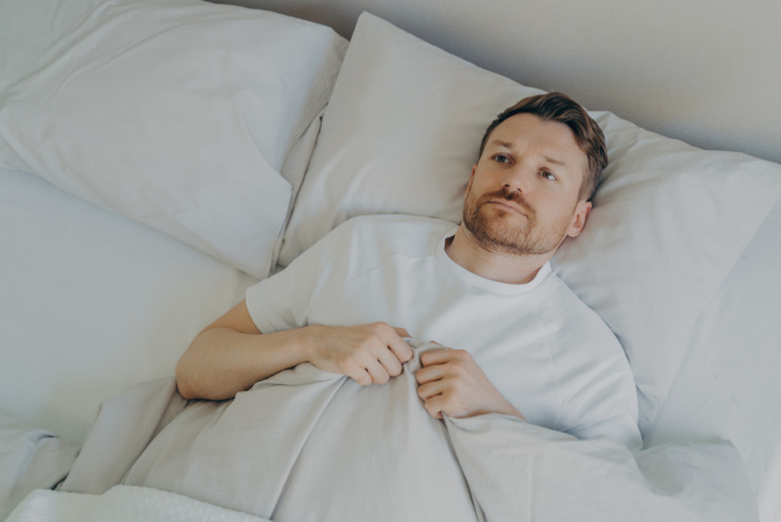 Junger Mann liegt nach dem Erwachen frustriert im Bett