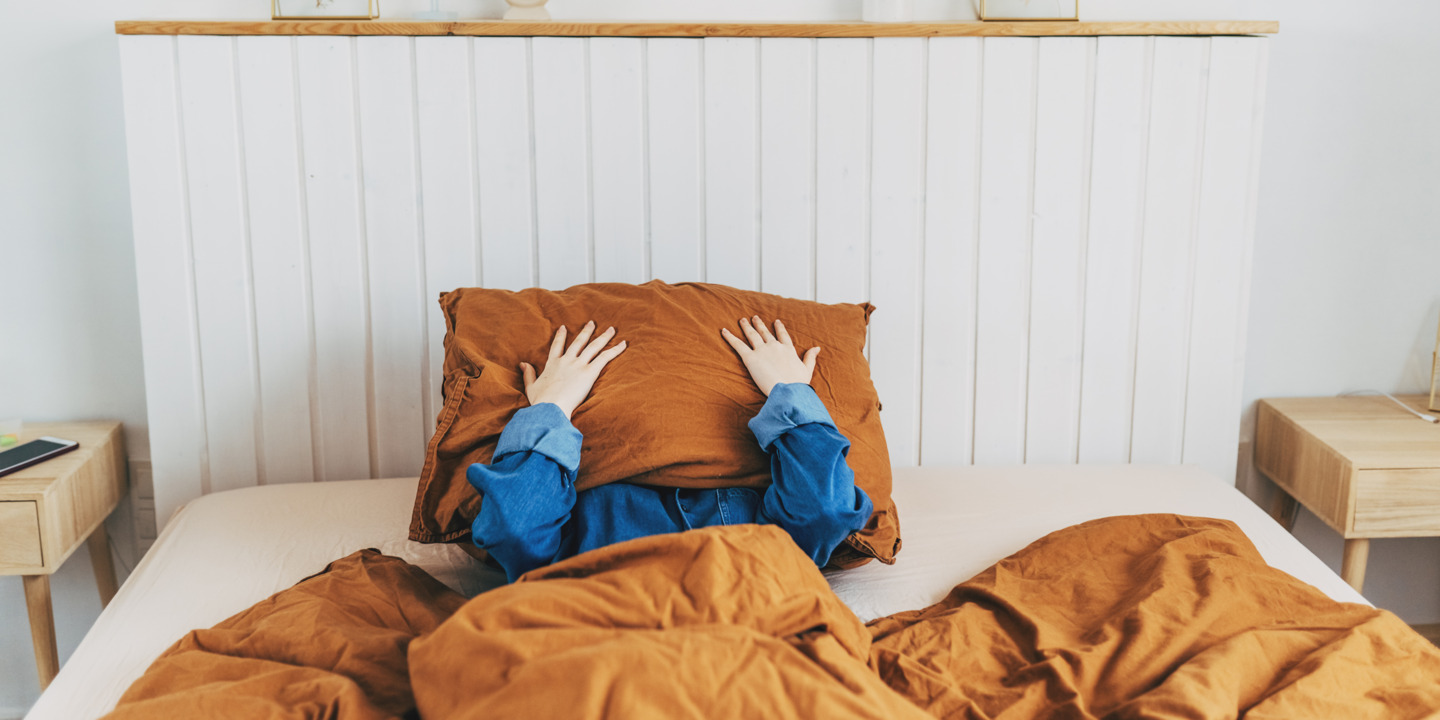 Person liegt im Bett und drückt sich ein Kissen ins Gesicht