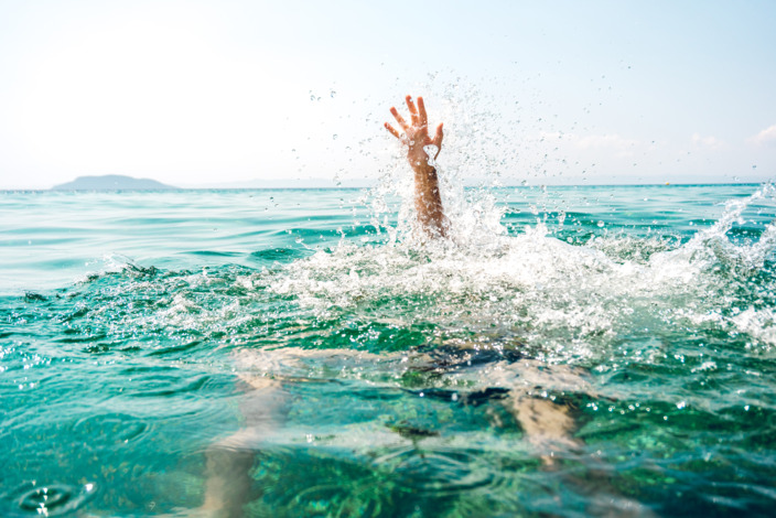 Eine schwimmende Person, die zu Ertrinken droht, streckt den Arm aus dem Wasser. 