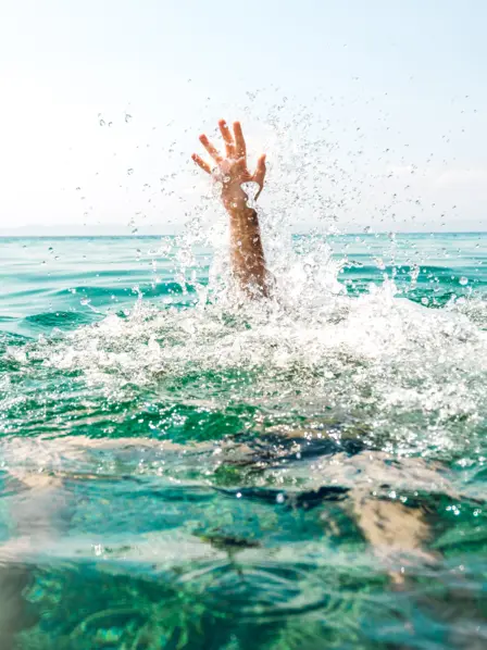 Eine schwimmende Person, die zu Ertrinken droht, streckt den Arm aus dem Wasser. 
