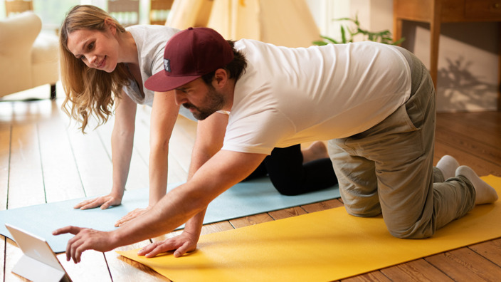 Mann und Frau auf Fitnessmatte vor dem Tablet. 