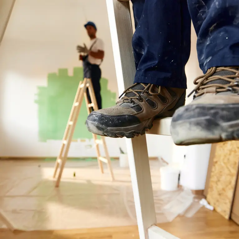Großaufnahme von den Sicherheitsschuhen eines Handwerkers, der auf einer Leiter steht.
