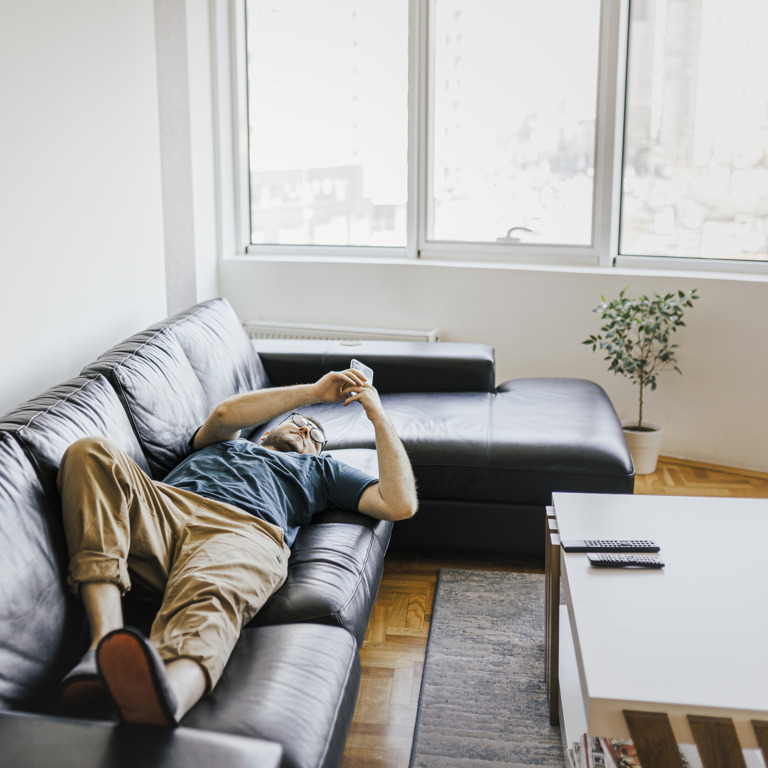 Mann liegt auf dem Sofa und schaut kopfüber in sein Smartphone