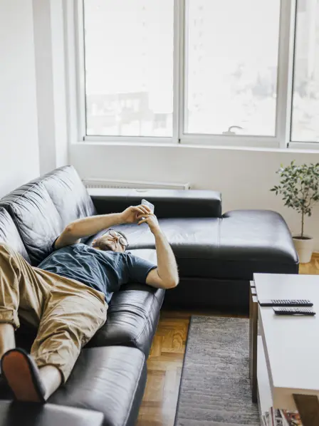 Junger Mann schaut in seine Smartphone auf einer Couch liegend