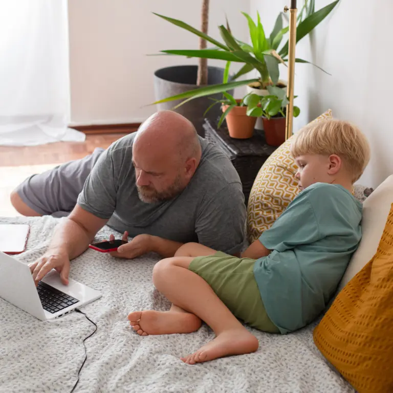 Vater und Sohn liegen im Bett und recherchieren am Laptop