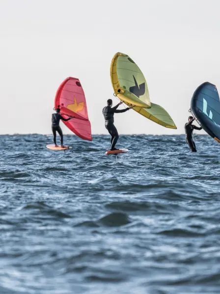 Drei Personen beim Wingfoilen auf einem See