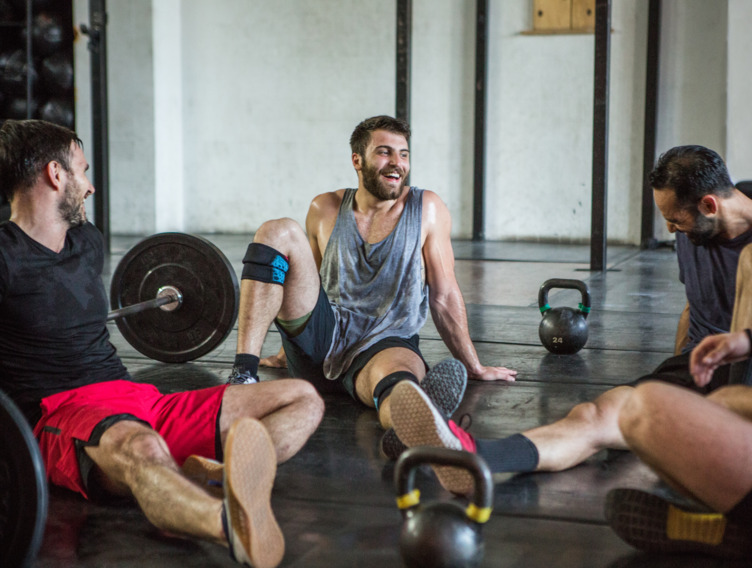 Drei Männer sitzen im Fitnessstudio auf dem Boden mit Gewichten zum Krafttraining um sie herum.